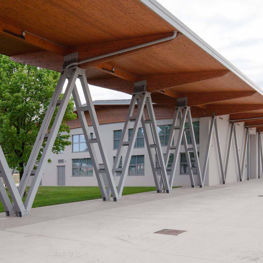 Cantilevered wooden roof panels supported by gray metal A-frame legs along a modern building exterior.